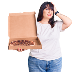 Young plus size woman holding delivery pizza box stressed and frustrated with hand on head, surprised and angry face