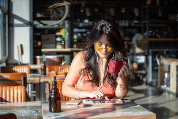 Woman listening to music with earphones while using a digital tablet and having coffee in a cafe.