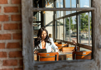 Reflection in the mirror of a woman using a digital tablet while sitting in a coffee shop.