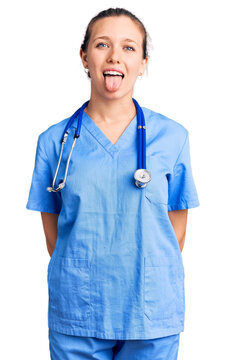 Young beautiful blonde woman wearing doctor uniform and stethoscope sticking tongue out happy with funny expression. emotion concept.