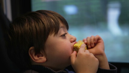 Little boy enjoying corn as a snack while traveling by train, passenger child eating food while staring at scenery pass by