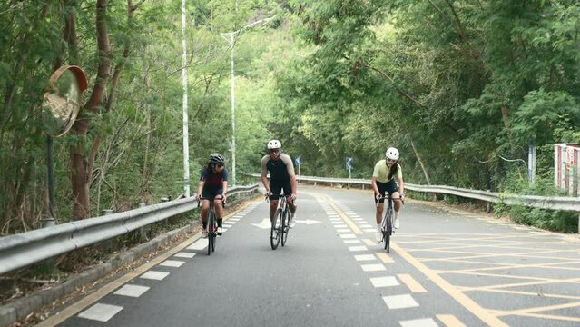 three young asian adults chatting while cycling on uphill rural road
