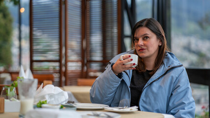 Beautiful young Latin American woman sitting in a restaurant with a cup of coffee in her hand with a thoughtful attitude