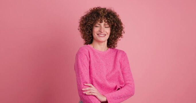 Smiling standing young curly haired woman on pink background