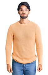 Handsome hispanic man wearing casual sweater puffing cheeks with funny face. mouth inflated with...