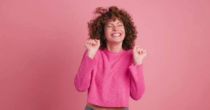 Excited young woman clapping hands and smiling on pink background