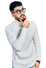 Young arab man with beard wearing elegant turtleneck sweater and glasses thinking worried about a question, concerned and nervous with hand on chin