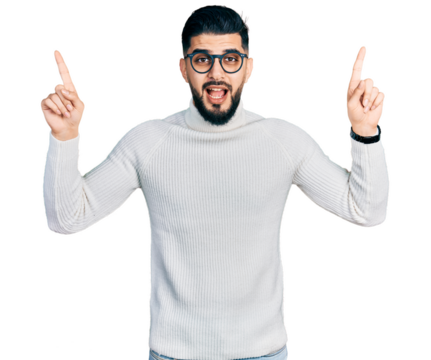 Young arab man with beard wearing elegant turtleneck sweater and glasses smiling amazed and surprised and pointing up with fingers and raised arms.