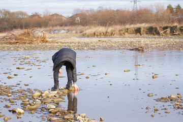 A man collects stones on the bank of a river in autumn.