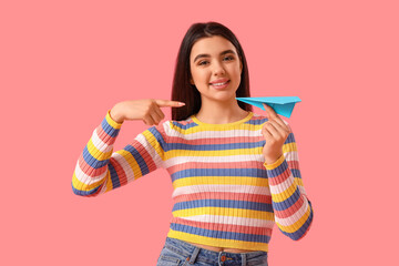 Young woman pointing at paper plane on pink background