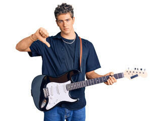 Young handsome man playing electric guitar with angry face, negative sign showing dislike with thumbs down, rejection concept
