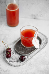 Cherry drink Kwas in a glass with fresh berries and a label on a light grey background. Refreshment summer drink. Healthy drink