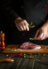 Cooking steak on the kitchen counter before frying or baking. The cook adds aromatic rosemary to beef meat