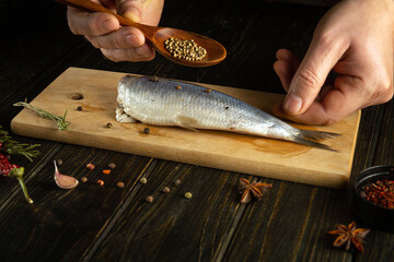 The chef prepares Atlantic herring on the kitchen table with pepper and coriander for a delicious...