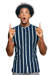 African american man with afro hair wearing casual clothes amazed and surprised looking up and pointing with fingers and raised arms.