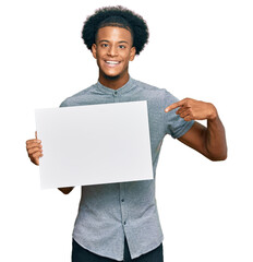 African american man with afro hair holding blank empty banner smiling happy pointing with hand and...