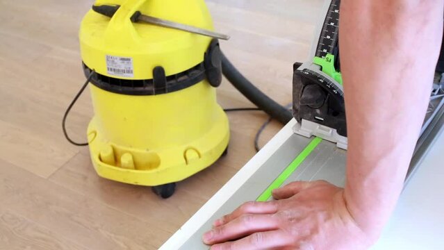 Man cuts-off edge of laminated chipboard with circular saw.