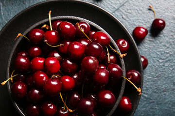 Bowl with sweet cherries on dark table