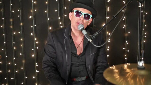 Man in glasses and black shirt is singing on studio with garlands