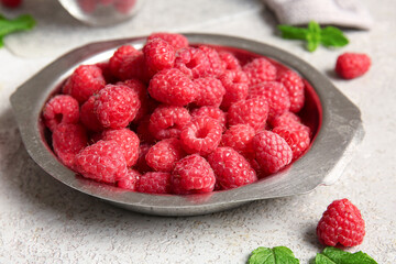 Metal plate with fresh raspberries and mint on grey background