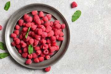 Plate with fresh raspberries and mint on grey background