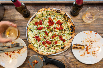 Male hand taking a slice of freshly baked Neapolitan zucchini pizza on a rustic wooden table in a traditional Pizzeria. - 710929124