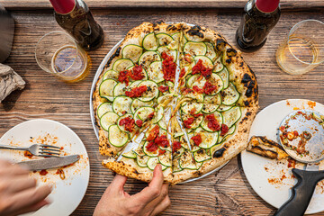 Male hand taking a slice of freshly baked Neapolitan zucchini pizza on a rustic wooden table in a traditional Pizzeria. - 710929183