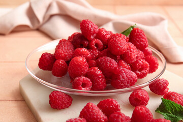 Glass plate with fresh raspberries and mint on pink tile table