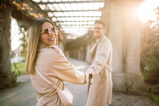 A stylish couple walks through the park in beige trench coats. A woman and a man spend time together in the spring at sunset. Concept of beauty, love and happiness.
