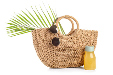 Wicker bag with stylish sunglasses, bottle of juice and palm leaf on white background