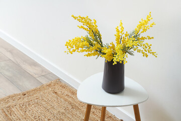 Vase with beautiful mimosa flowers on end table near white wall, closeup