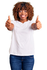 Young african american woman wearing casual white tshirt approving doing positive gesture with hand, thumbs up smiling and happy for success. winner gesture.