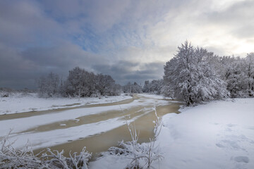 Winter landscape, a river covered with ice and snow, a beautiful sky with clouds against the...
