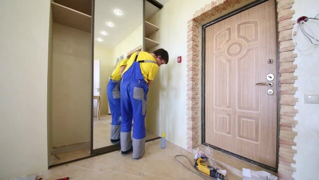 worker checks quality of mounting sliding wardrobe mirrored door.