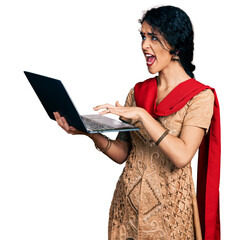 Young indian woman working using computer laptop angry and mad screaming frustrated and furious, shouting with anger looking up.