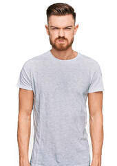 Young redhead man wearing casual grey t shirt puffing cheeks with funny face. mouth inflated with air, crazy expression.