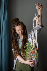 Young woman with dreadlocks holding homeplant decor from cotton thread macrame. 
