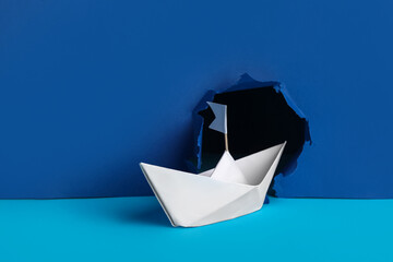 White origami boat with flag punching blue wall