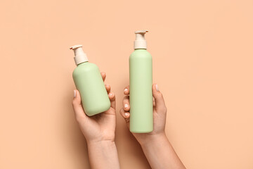 Female hands with bottles of cosmetic products on color background, closeup