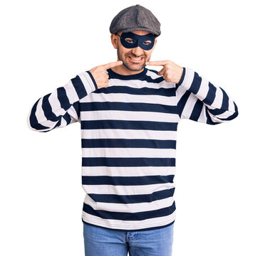 Young handsome man wearing burglar mask smiling cheerful showing and pointing with fingers teeth and mouth. dental health concept.