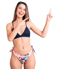 Young beautiful girl wearing bikini smiling and looking at the camera pointing with two hands and fingers to the side.