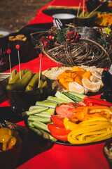 Autumn picnic table laden with fresh pickles, crisp vegetables, citrus fruit, and festive wreath on vivid red cloth