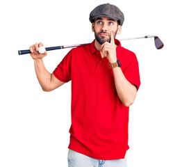 Young handsome man with beard playing golf holding club and ball serious face thinking about...