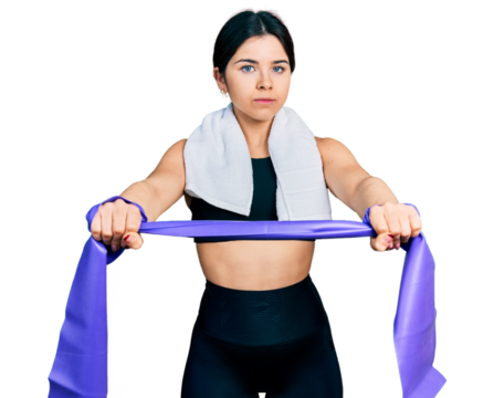 Young brunette woman with blue eyes training arm resistance with elastic arm bands relaxed with serious expression on face. simple and natural looking at the camera.