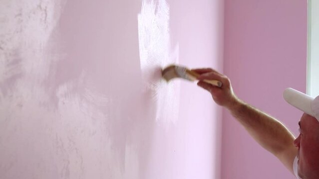 Builder on white cap with a brush in hand is painting walls 