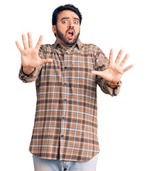 Naklejka premium Young hispanic man wearing casual clothes afraid and terrified with fear expression stop gesture with hands, shouting in shock. panic concept.