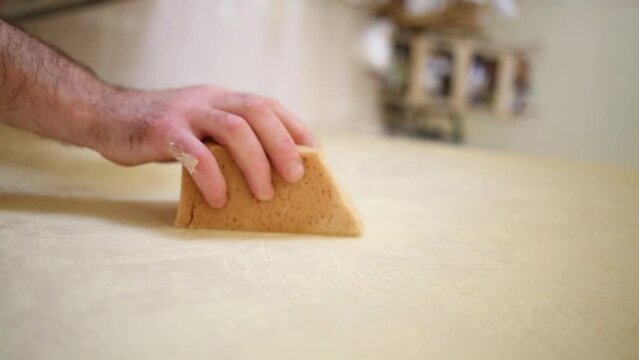 Builder is polishing a yellow plaster wall using sanding sponge.