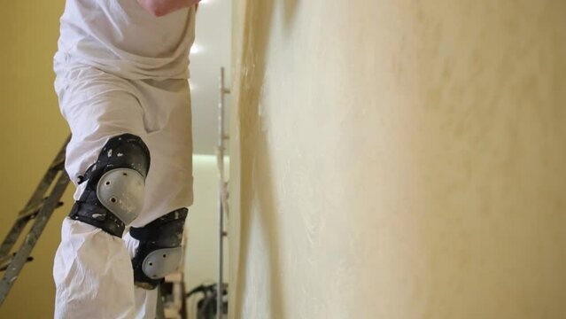 Builder is standing on the scaffold and polishing wall 