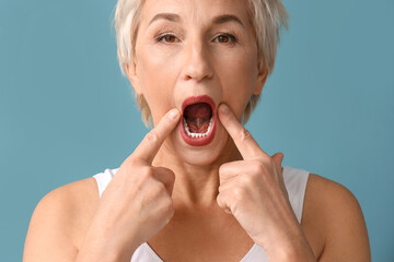 Mature woman doing face building exercise on blue background, closeup