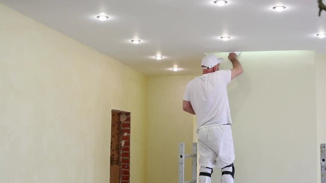 Worker is fixing the yellow wall near ceiling using pallet.